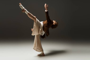 Kıvırcık saçlı genç bir adam atletizmi bir stüdyoda enerjik bir dansla sergiliyor..