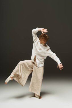 Kıvırcık saçlı genç bir dansçı minimalist bir stüdyoda akışkan hareketler sergiliyor..