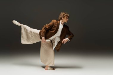 Kıvırcık saçlı dansçı dinamik stüdyo ortamında atletik hareketler sergiliyor.