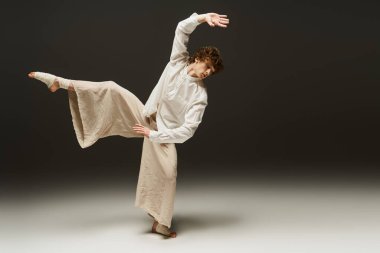 Kıvırcık saçlı genç bir adam stüdyo ortamında anlamlı bir dans gösterisi sergiliyor..