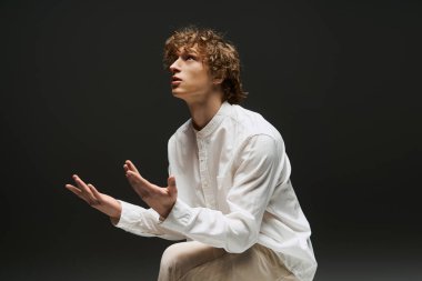 Genç kıvırcık saçlı bir adam tutkulu bir şekilde minimalist bir stüdyoda dans ediyor ve atletizmini gösteriyor..