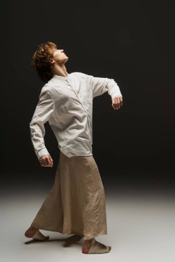 Kıvırcık saçlı genç dansçı dans stüdyosunda akışkan hareketler sergiliyor..