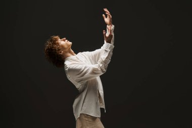 Dramatik bir stüdyoda kıvırcık saçlı genç bir adam dans hareketlerini tutkuyla sergiliyor..