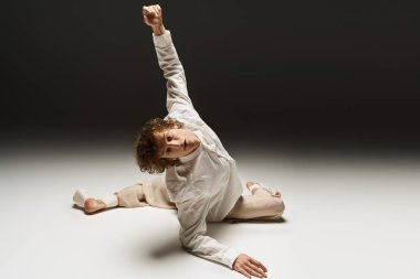 Kıvırcık saçlı genç bir adam iyi aydınlatılmış bir stüdyoda açıkça dans ediyor, yeteneğini sergiliyor..