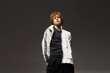 Kıvırcık saçlı genç bir adam yeteneklerini bir stüdyoda dinamik dans hareketleri yoluyla sergiliyor..