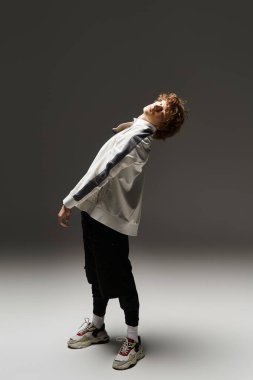 Kıvırcık saçlı genç bir adam atletik dansını şık bir stüdyoda sergiliyor..