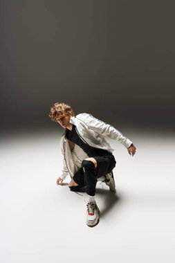 Kıvırcık saçlı genç bir adam dans yeteneklerini geniş bir stüdyoda sergiliyor, enerji saçıyor..