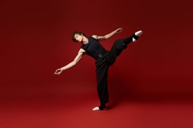 Genç bir kıvırcık adam dans yeteneğini kırmızı renklerle dolu canlı bir stüdyoda sergiliyor..