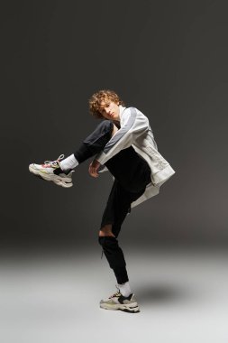 Genç kıvırcık saçlı bir adam modern bir stüdyoda dans ederken ritmini ve enerjisini ifade eder..