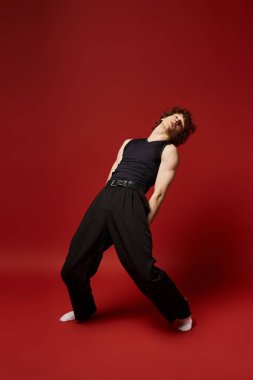 Genç kıvırcık saçlı bir dansçı canlı kırmızı stüdyo ortamında dinamik hareketler sergiliyor..