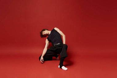 Kıvırcık saçlı genç bir dansçı dinamik bir şekilde kırmızı bir arka planda hareket eder..