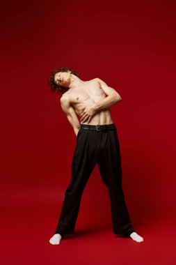 Kıvırcık saçlı genç bir adam canlı kırmızı bir stüdyoda dans ederek enerjisini sergiliyor..