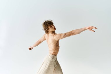 Kıvırcık saçlı genç bir adam gri arka planda zarif bir şekilde dans ediyor, atletik yeteneklerini sergiliyor..
