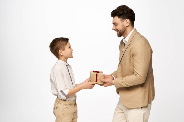 A young boy joyfully presents a wrapped gift to his smiling father during a heartfelt celebration.