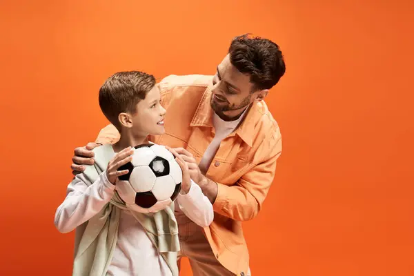 A joyful father and son share a special moment while holding a soccer ball, surrounded by warmth.