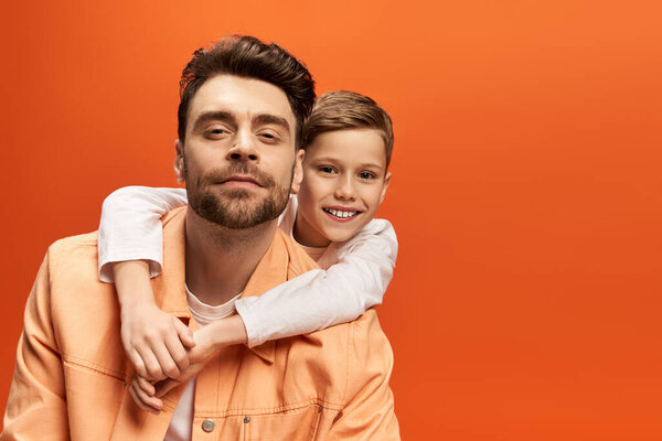 A father and son share a joyful moment, celebrating their bond against a vibrant orange backdrop.
