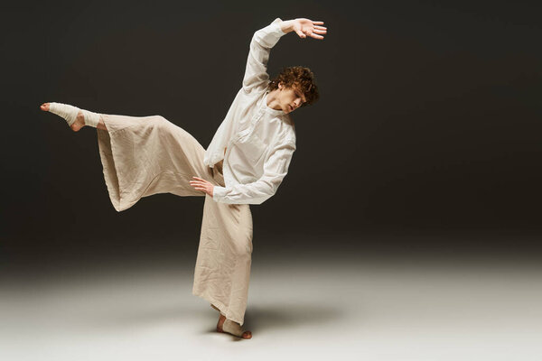 A young man with curly hair performs an expressive dance move in a studio setting.