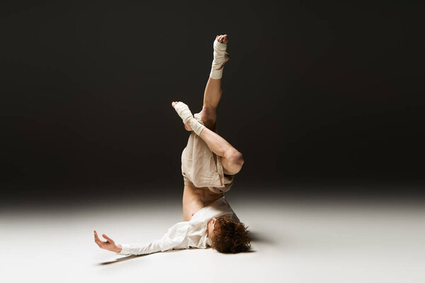 Curly-haired young man performs an energetic dance routine in a modern studio space.