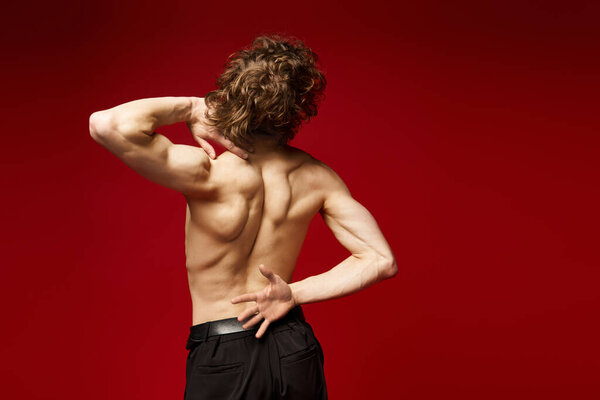 A young curly man expresses himself through dance, radiating energy in a red studio.