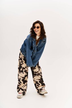 Genç bir kadın, modaya uygun inek desenli pantolon ve kot ceketle kendinden emin poz veriyor..