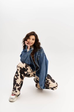 Modaya uygun genç bir kadın, stüdyo odasında inek desenli pantolon ve kot ceketiyle tarzını sergiliyor..