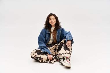 Gri arka planda inek desenli pantolonu olan genç bir kadın modaya uygun kıyafetini gösteriyor..