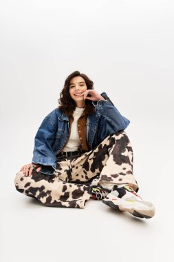 Moda desenli inek desenli pantolonlu genç bir kadın stüdyoda rahat bir şekilde otururken gülümsüyor..