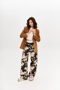 Kendine güvenen genç bir kadın, gri bir zemine karşı şık inek desenli pantolonla poz veriyor..