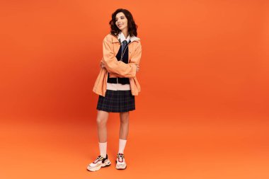 Kollarını kavuşturmuş genç bir kadın şık bir etek ve ceket sergiliyor..