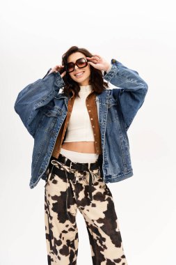 Genç bir kadın, gri bir zemine karşı inek desenli pantolonuyla şık bir kıyafetle rahatça poz veriyor..