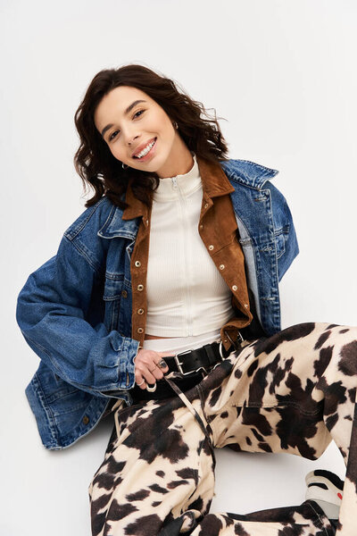Модная молодая женщина уверенно позирует в штанах для печати коровы и стильной куртке, улыбаясь.