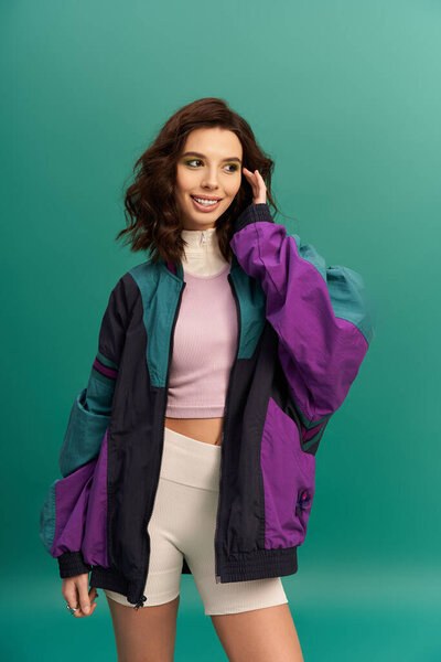 A fashionable young woman showcases a sporty look with confidence against a vibrant background.