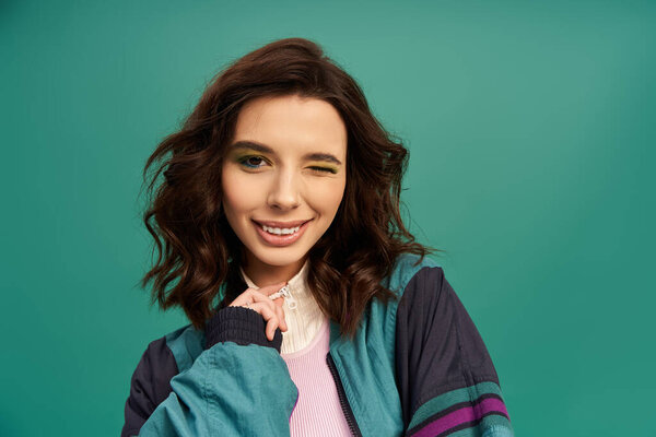 Stylish young woman winks playfully while showcasing trendy sporty attire in a vibrant studio.