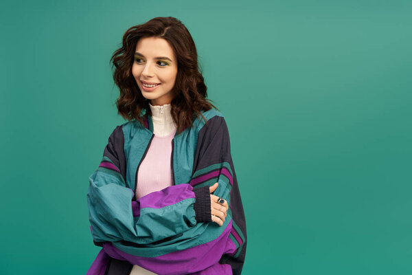 A young woman stands confidently in a trendy sporty outfit, smiling against a turquoise background.