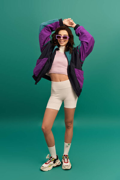 A young woman models a trendy sporty outfit exuding confidence against a turquoise backdrop.