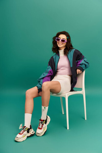 A stylish young woman poses confidently in a sporty outfit against a turquoise backdrop.