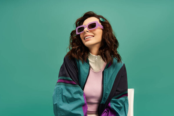 Young woman showcases a chic sporty outfit with bold sunglasses, posing confidently in a studio.