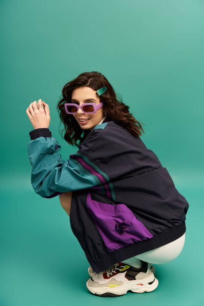 A young woman in a sporty outfit exudes confidence against a vibrant turquoise background.