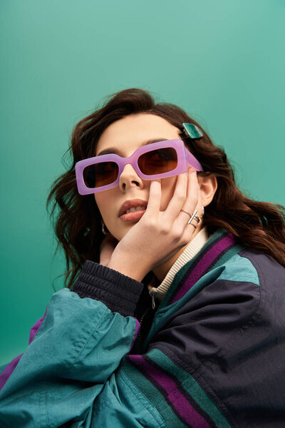 A young, fashionable woman showcases her sporty outfit with trendy sunglasses in a studio.