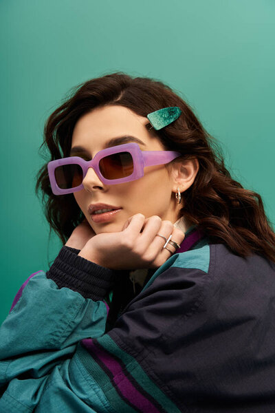 Sporty stylish woman poses confidently against a bright turquoise backdrop while wearing sunglasses.