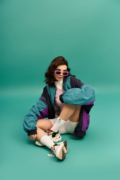 Young woman exudes confidence in fashionable sporty attire while seated in a studio.