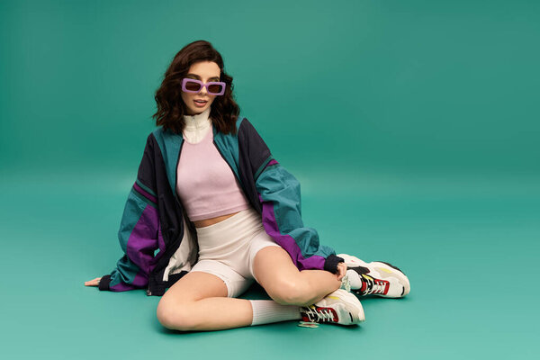 A confident young woman in a sporty outfit poses against a vibrant turquoise backdrop.