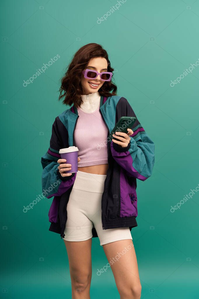 A young woman in a trendy sporty outfit checks her phone while holding a cup, radiating style.