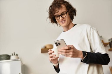 Genç bir adam evinde rahat, rahat giyinmiş telefonuyla kayıyor..