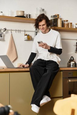 Genç bir adam evinde rahat giysiler içinde uzanır, akıllı telefonuyla biraz zaman geçirir..