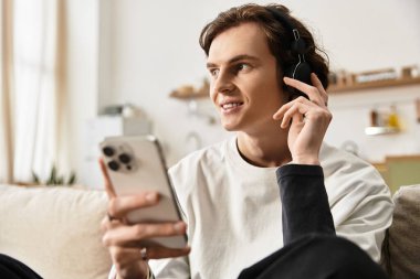 Genç bir adam evde rahat rahat oturup kulaklıklarıyla müzik dinliyor..