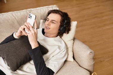 Genç bir adam rahat bir şekilde kanepede uzanır, akıllı telefonuyla meşgul olur, rahat giyinir..