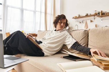 Genç adam evdeki bir kanepede dinleniyor, kendini kitaplara kaptırmış ve gündüzleri rahat bir ortamda..