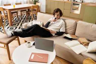 Genç bir adam gündelik bir şekilde kanepede oturur, notlar üzerinde düşünür ve evde huzurlu bir öğleden sonranın tadını çıkarır..