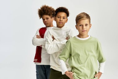 Üç çocuk, modaya uygun kıyafetleriyle, benzersiz tarzlarını sergileyerek güvenle duruyorlar..